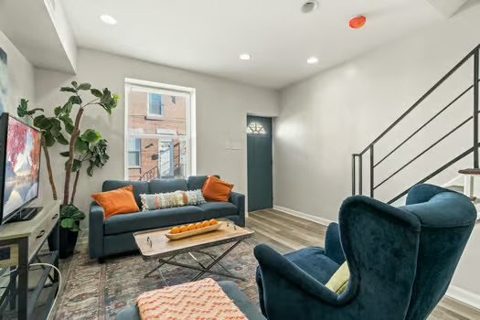 Furnished living room with a teal sofa, orange pillows and a staircase